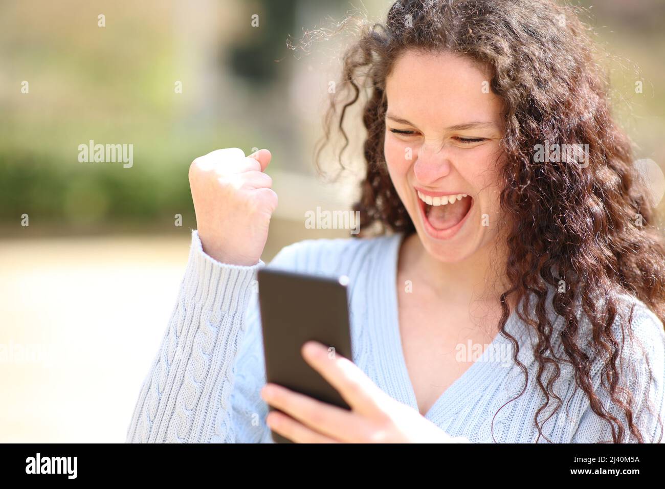 Donna entusiasta che festeggia le buone notizie controllando lo smartphone in un parco Foto Stock