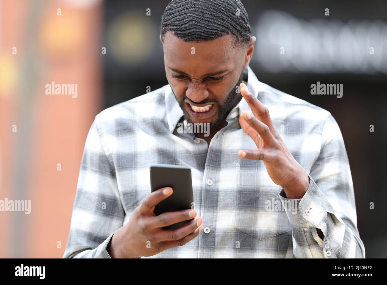Vista frontale ritratto di un uomo arrabbiato con pelle nera controllo telefono problema in strada Foto Stock