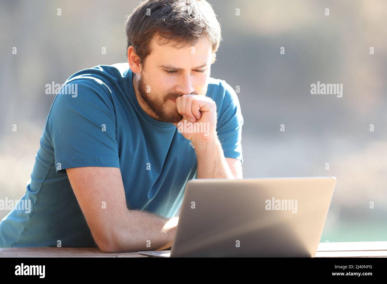 Uomo pensivo che controlla i contenuti del laptop all'aperto in natura Foto Stock