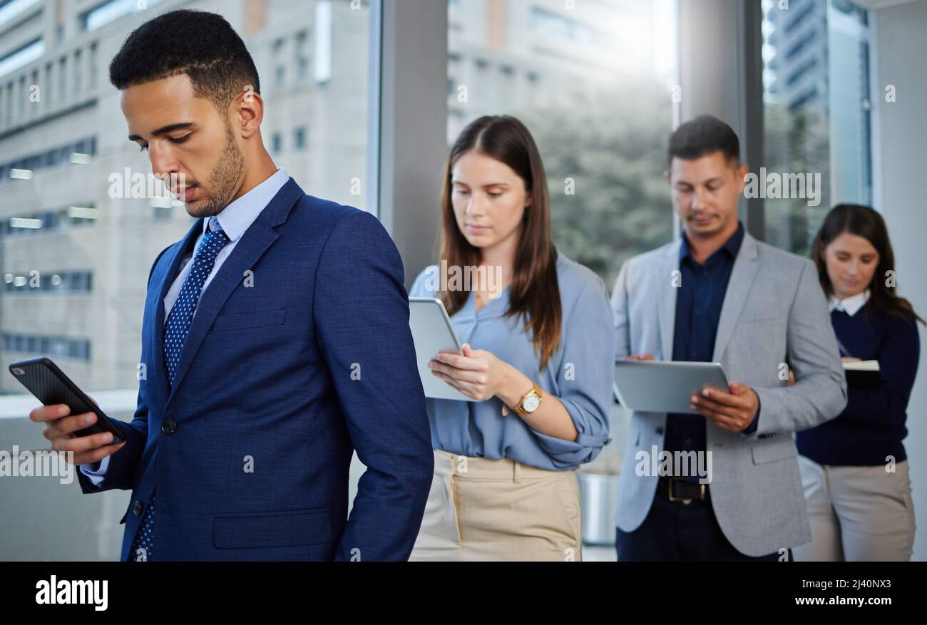 Il futuro del mondo degli affari. Scatto di un gruppo di operatori che utilizzano dispositivi digitali mentre sono in attesa in linea. Foto Stock