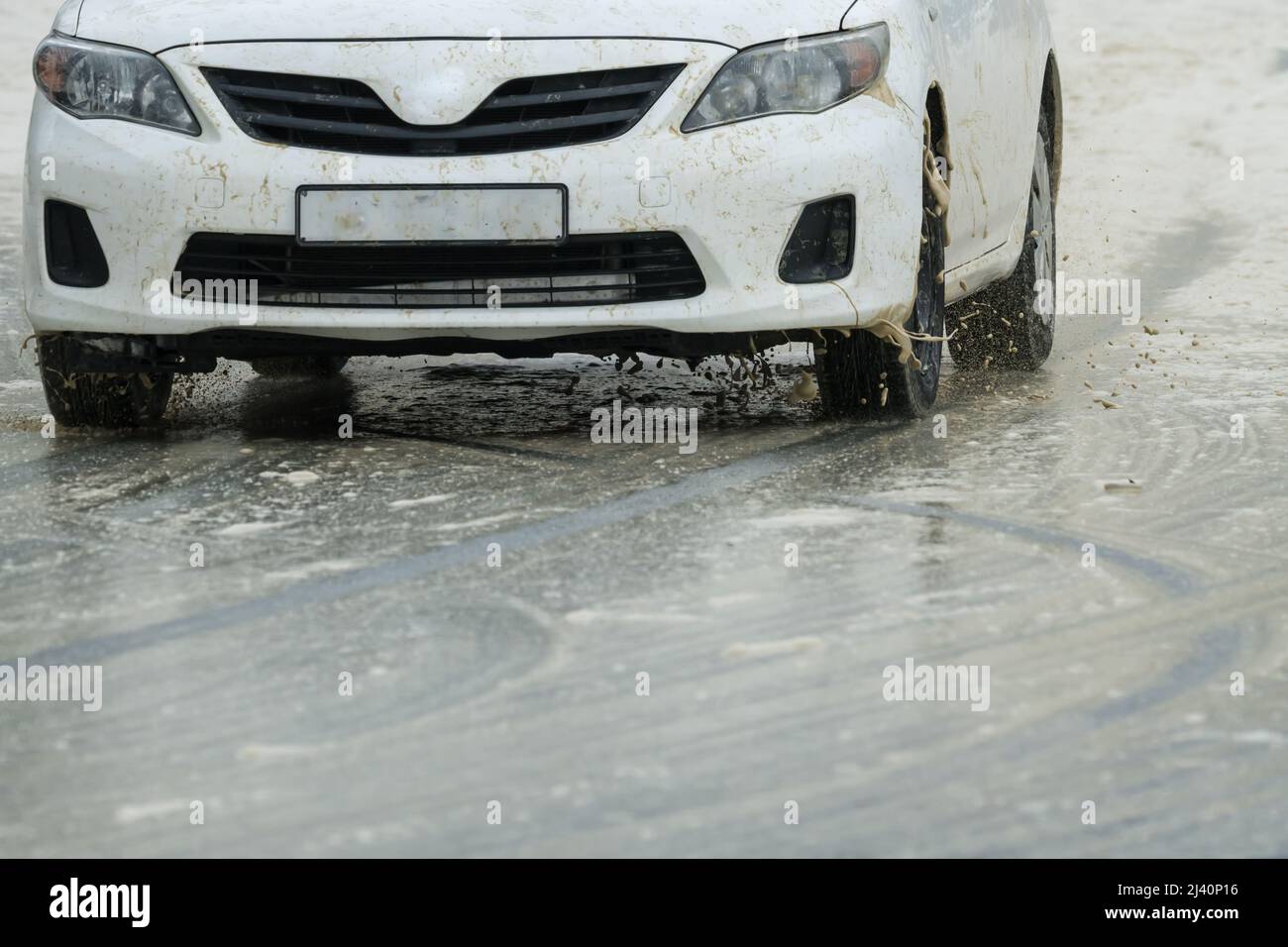 Primo piano di una vettura bianca ruote anteriori che guidano su una strada scivolosa bagnata durante un inverno tempesta concetto di tempo e sicurezza stradale Foto Stock