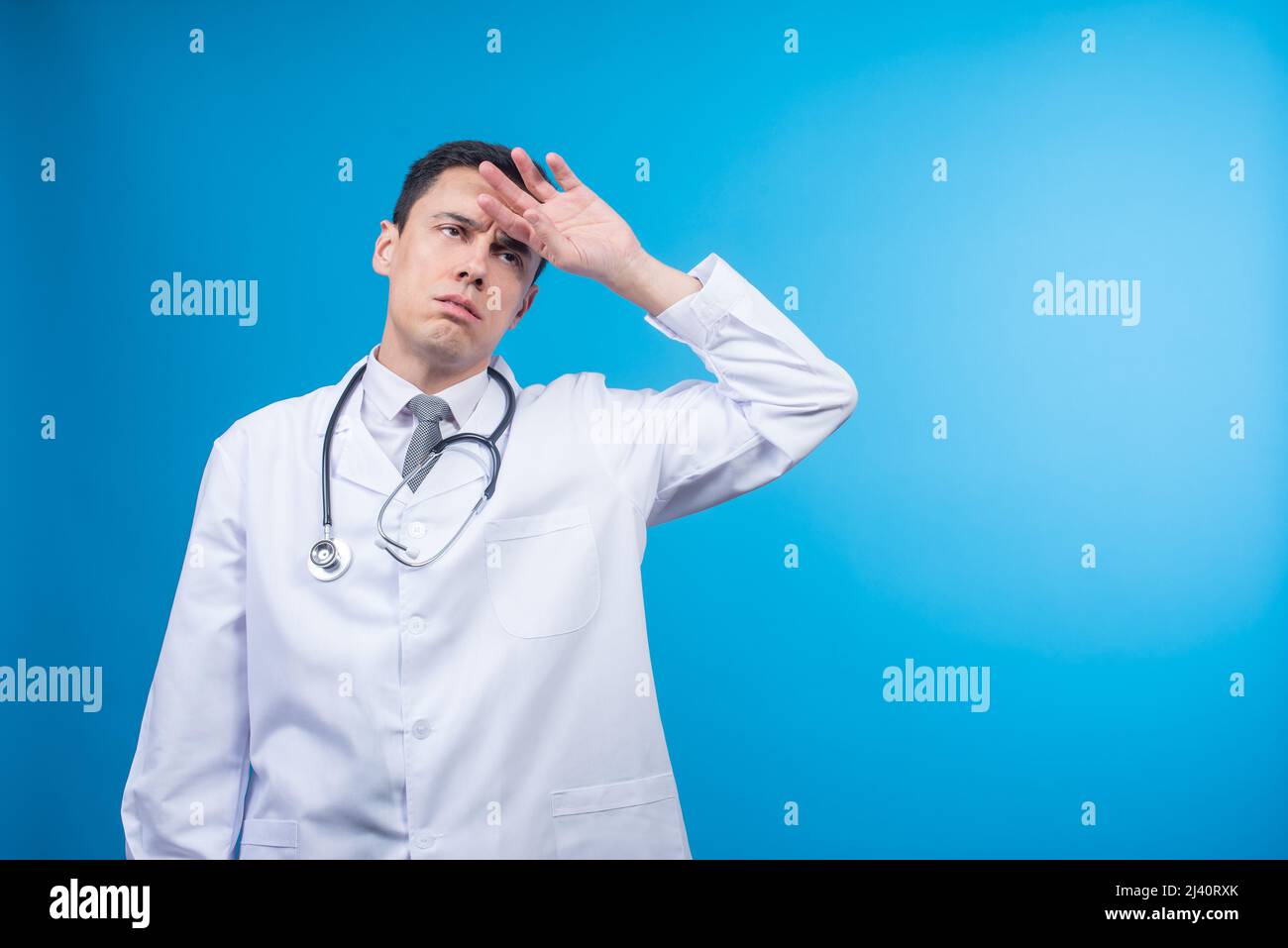 Medico maschile esausto che tocca la fronte in studio Foto Stock