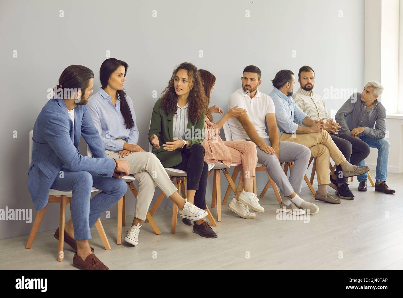 Gruppi di persone diverse che parlano tra loro mentre si siedono in fila in sala d'attesa Foto Stock