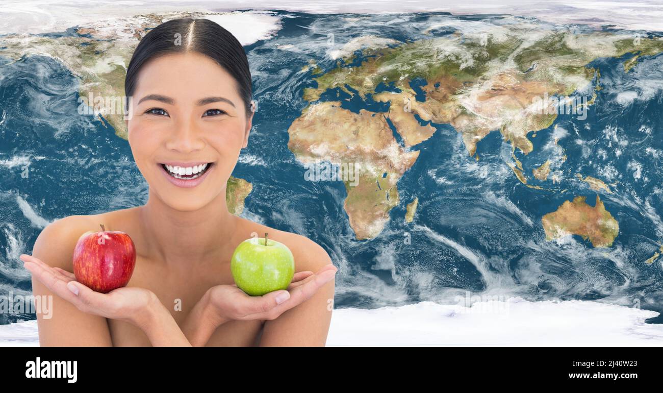 Ritratto di donna asiatica che tiene due mele contro la mappa del mondo sullo sfondo Foto Stock