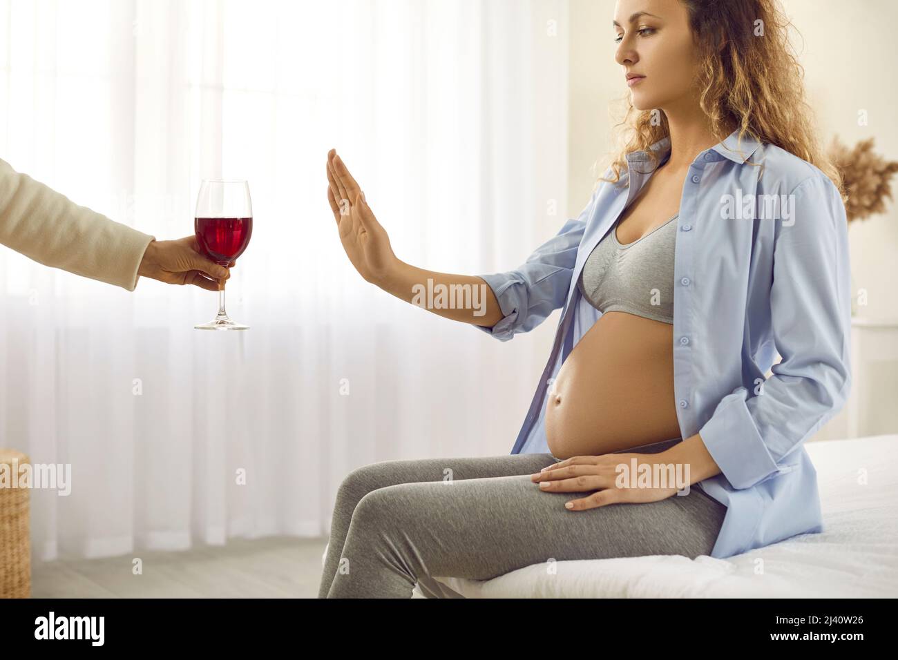 Alla donna incinta viene offerto un bicchiere di vino che fa un gesto di arresto e rifiuta di bere Foto Stock