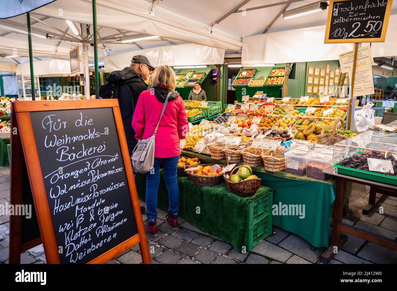 Monaco di Baviera, Germania - 5 novembre 2019: Due persone alla ricerca di prodotti presso il locale negozio di frutta con lavagna a mano in lingua tedesca dettagli prodotti Foto Stock