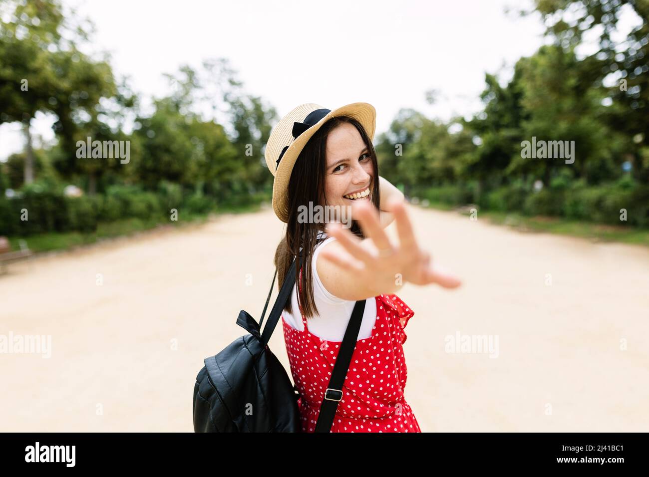 Felice giovane donna che si allunga la mano alla macchina fotografica e sorride nel parco pubblico Foto Stock