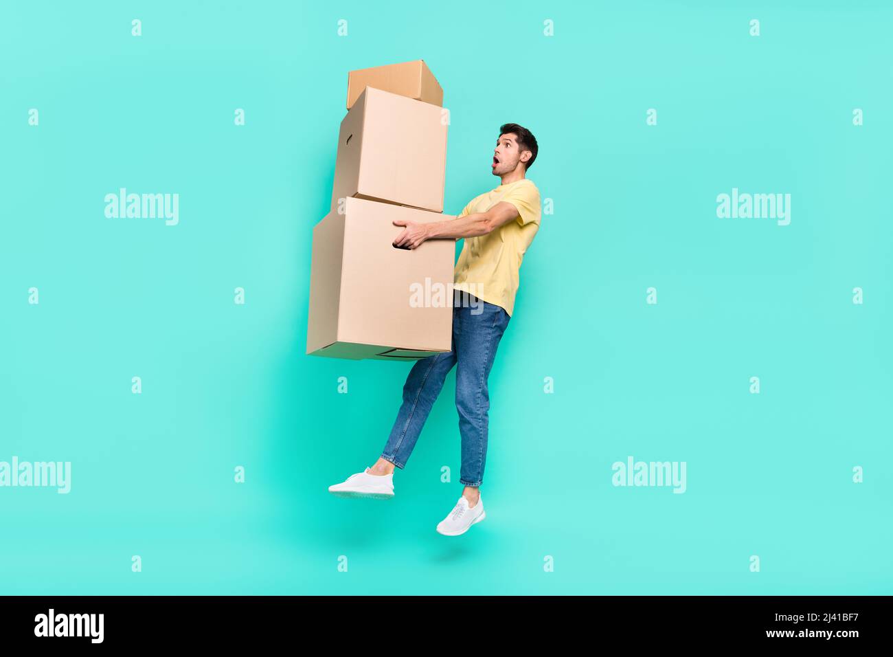 Foto del corpo intero di tipo brunet impressionato salto con scatola indossare t-shirt scarpe jeans isolato su sfondo turchese Foto Stock