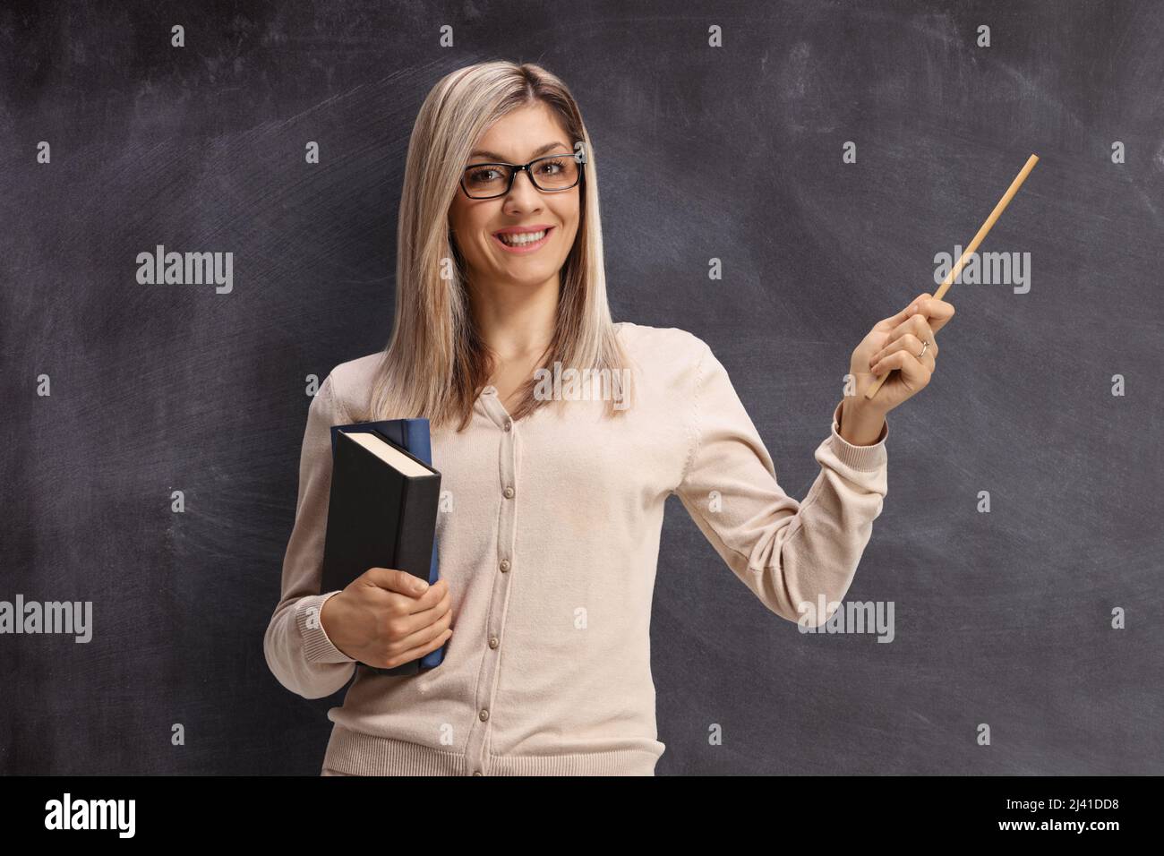 Insegnante di sesso femminile in piedi di fronte a una lavagna e puntando con un bastone Foto Stock
