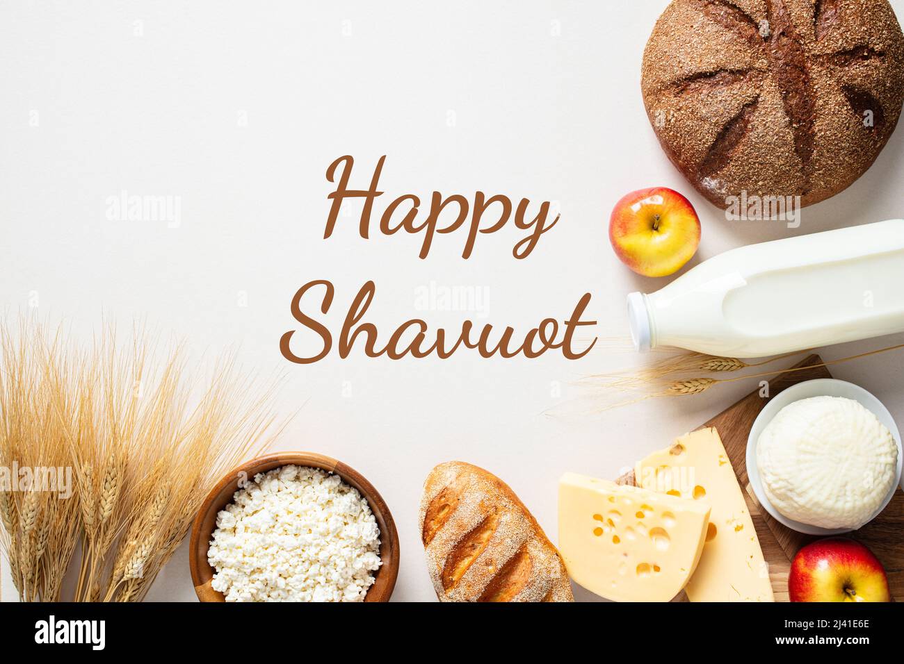 Happy Shavuot biglietto d'auguri, banner, poster. Sfondo ebraico vacanza. Latticini, bottiglia di latte, formaggio casereccio, pane, formaggio, mele, grano o Foto Stock