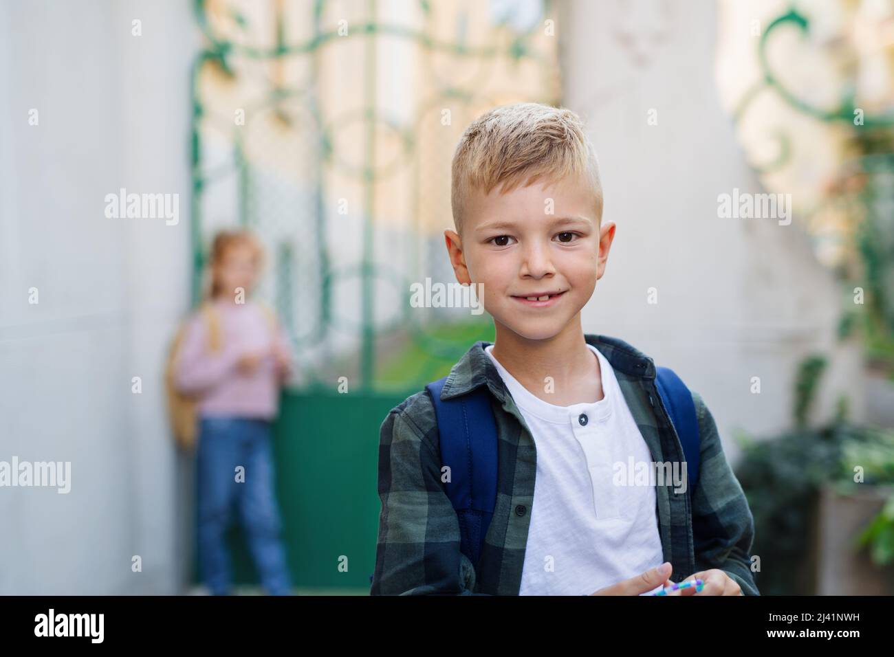 Ragazzo piccolo felice che guarda la macchina fotografica di fronte alla scuola. Foto Stock
