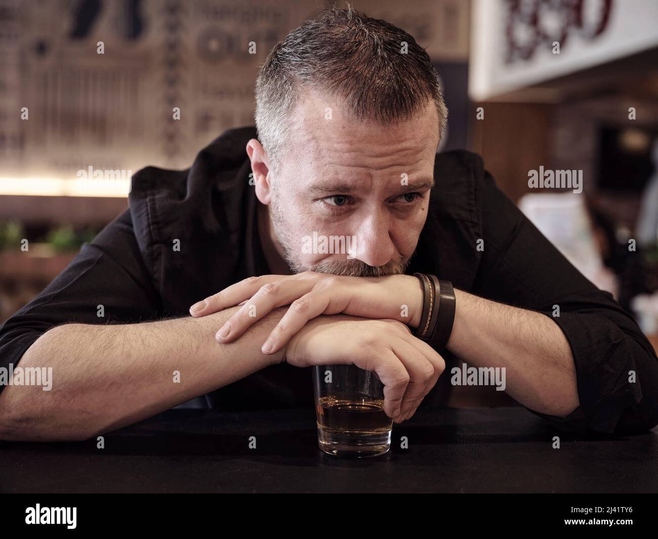 Ubriaco cliente maschio appoggiandosi le mani su un bicchiere di whiskey al pub. Dipendenza da alcol, depressione e problema di bere. Foto Stock