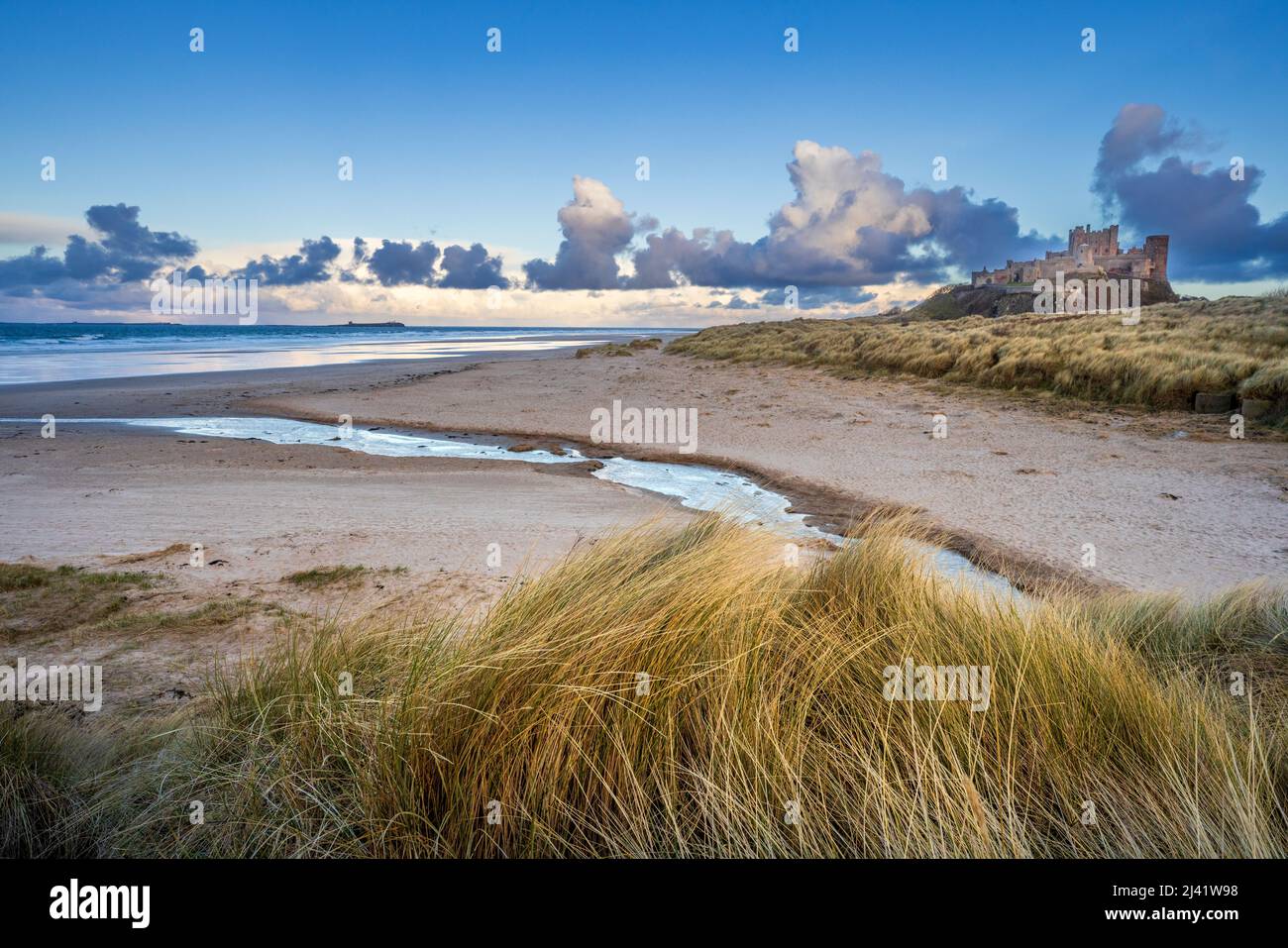 Mill Burn che scorre nella spiaggia di Bambburgh con il castello sullo sfondo, Northumberland, Inghilterra Foto Stock
