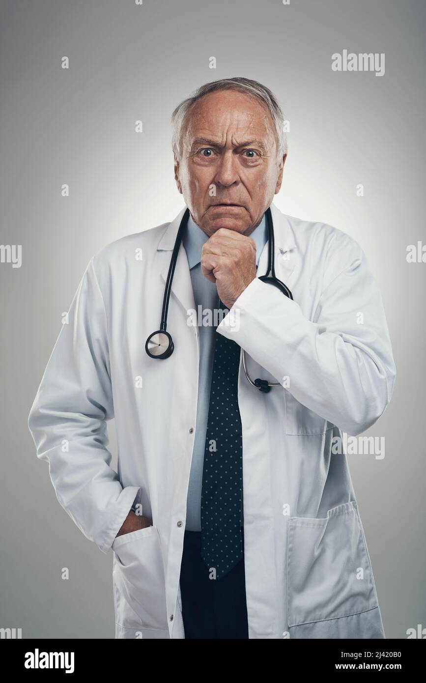Salvare la giornata è un lavoro serio. Scatto di un medico anziano di sesso maschile in uno studio su sfondo grigio. Foto Stock