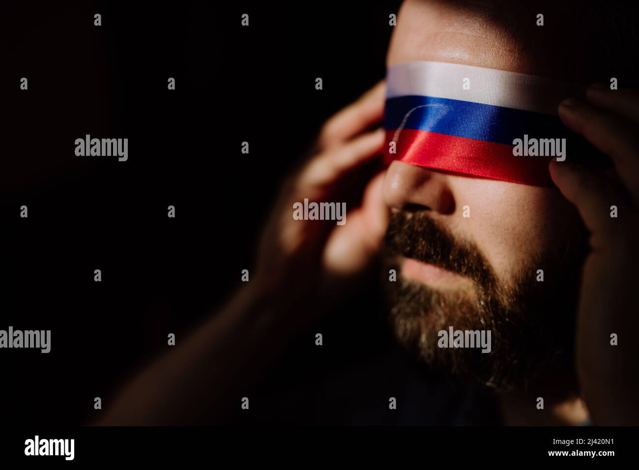 Uomo con bandiera russa cieca su sfondo nero, propaganda russa ha chiuso il concetto degli occhi della gente. Foto Stock