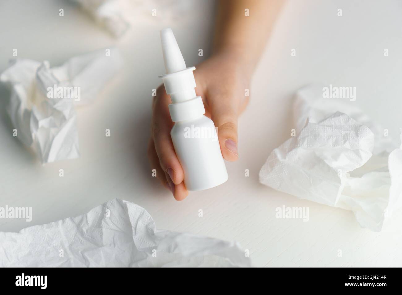 Il bambino tiene le mani del flacone di medicinale spray sul naso su un tavolo bianco con un tessuto di carta. Trattamento con naso che cola Foto Stock