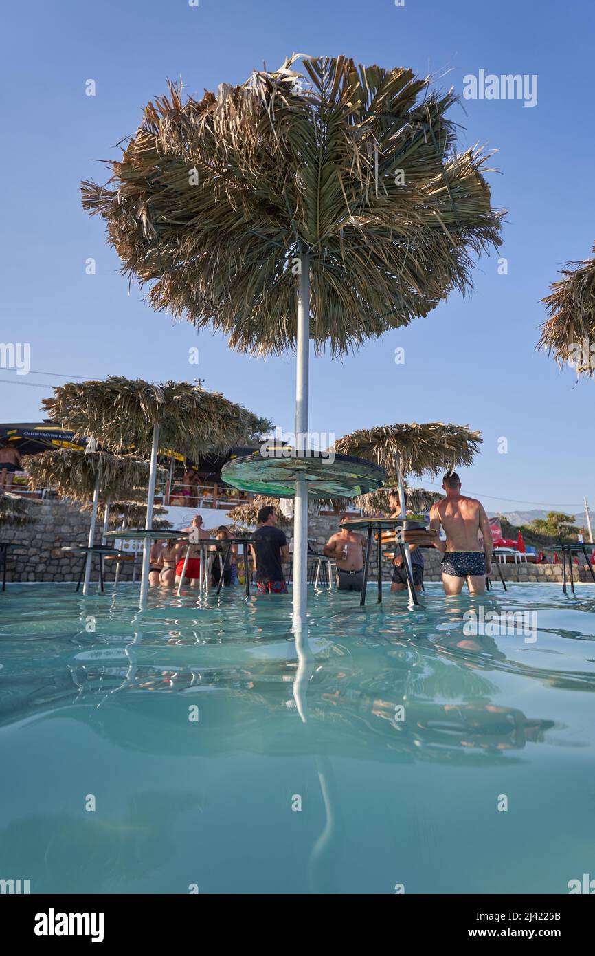BUDVA, MONTENEGRO - 30 LUGLIO 2021: Un tavolo con un ombrello fatto di foglie di palma in un bar sulla spiaggia Ploce in piscina Foto Stock