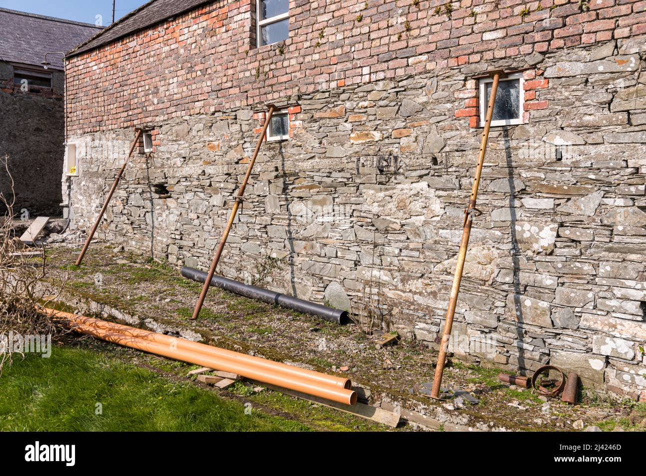Pali per ponteggi tengono il muro di un antico edificio agricolo. Foto Stock