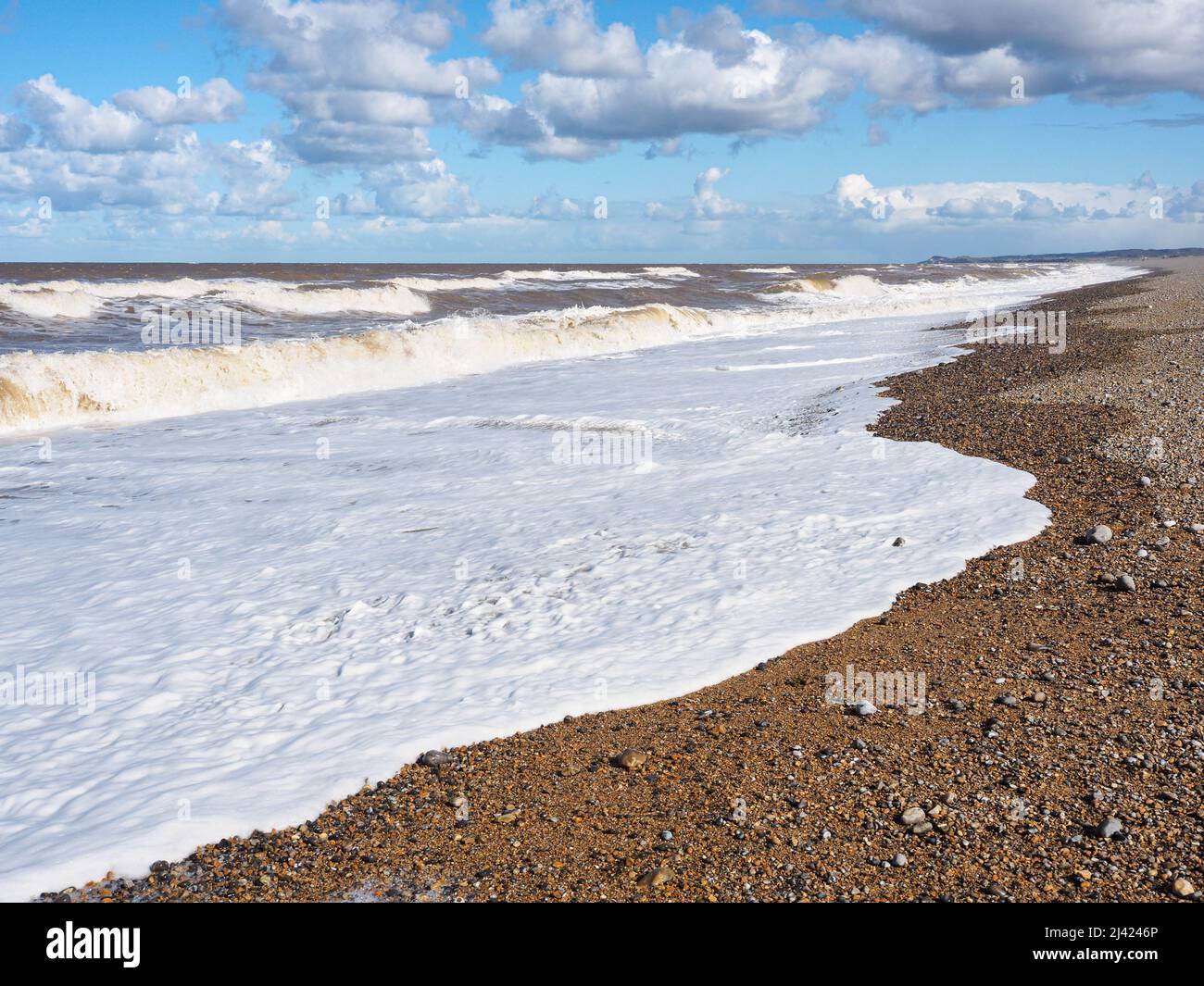 Le onde si infrangono sulla spiaggia sotto il cielo blu e le nuvole bianche, Blakeney Point, Norfolk Foto Stock