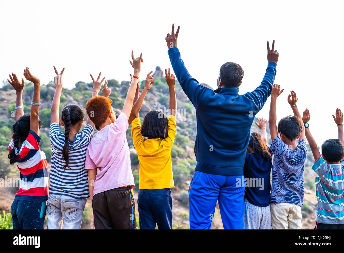 Back view shot di gruppo di ragazzi adolescenti con insegnante che festeggia sollevando le mani in cima alla collina dopo aver raggiunto la destinazione - concetto di estate Foto Stock