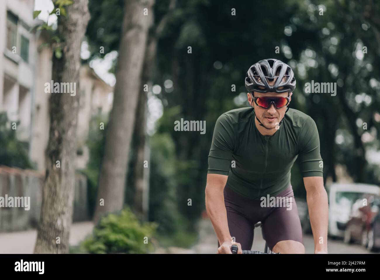 Forte atleta maschile in abbigliamento sportivo, casco e vetrine in bicicletta sulla strada della città. Uomo caucasico che trascorre del tempo libero per praticare attività all'aperto. Healt Foto Stock