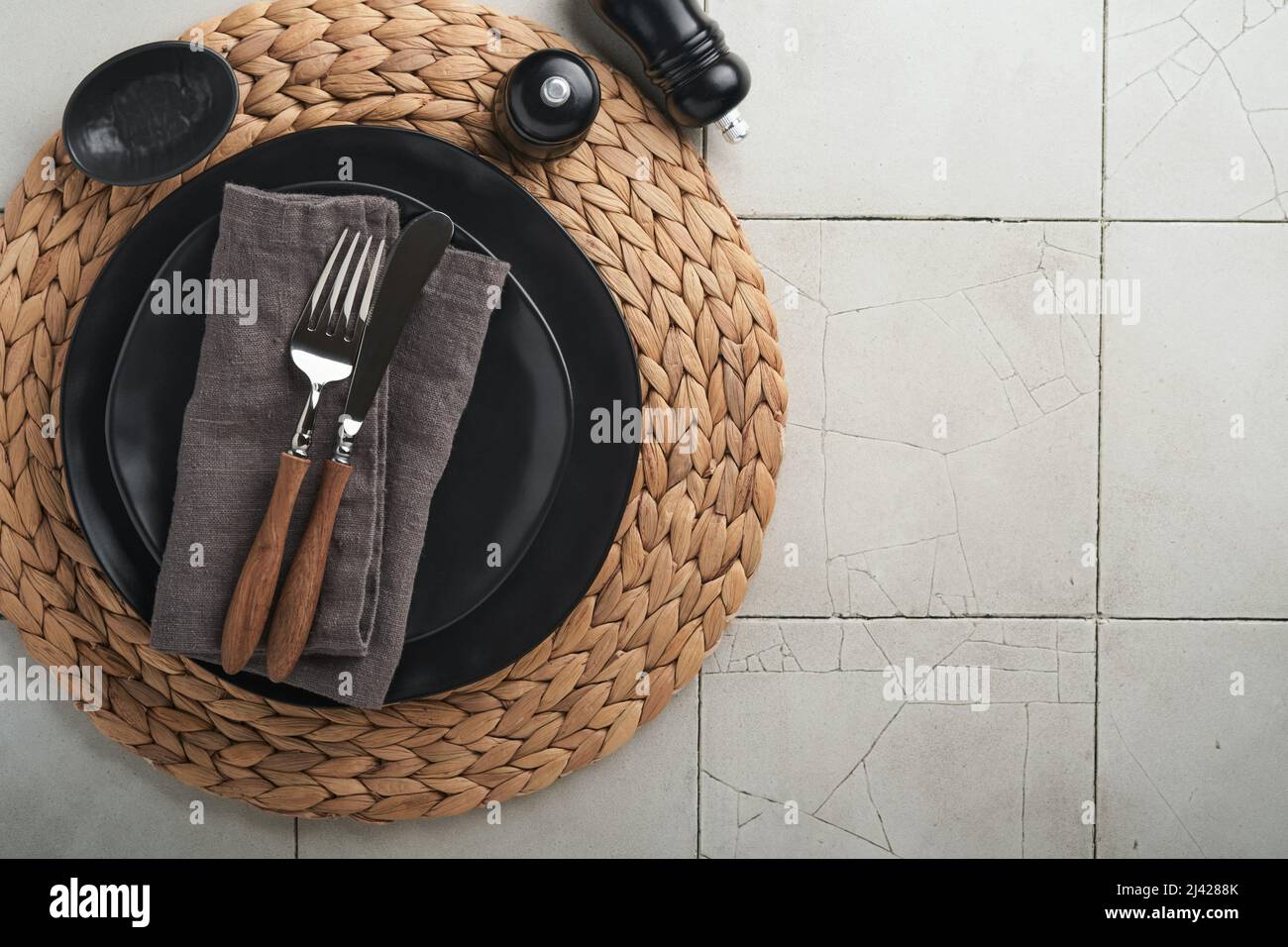 Piastra nera vuota in ceramica, argenteria e biancheria da cucina tovagliolo su sfondo vecchio tavolo piastrelle in ceramica. Pietra di cottura sfondo. Vista dall'alto con copia Foto Stock