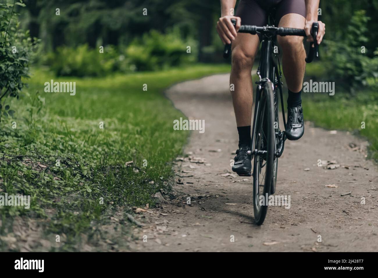 Primo piano del ciclista professionale con forti gambe muscolari in bicicletta al verde parco estivo. Concetto di persone, sport e hobby attivo. Foto Stock