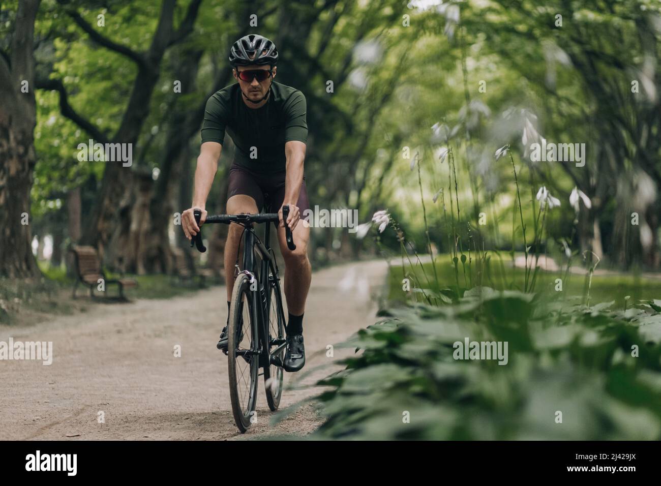 Giovane uomo sportivo in casco di sicurezza e occhiali che pratica in bicicletta nel verde parco della città. Concetto di attività estiva e formazione regolare. Foto Stock