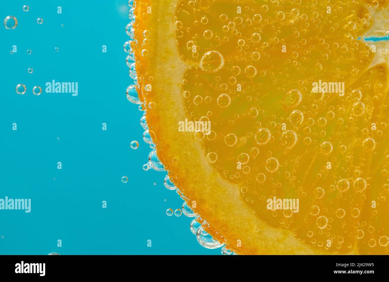 primo piano di una fetta arancione sospesa in liquido che mostra bolle su sfondo blu chiaro Foto Stock