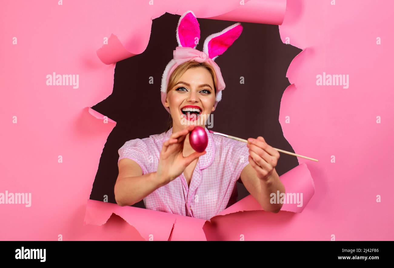 Donna felice in falso coniglietto orecchie pittura uovo di pasqua. Ragazza di coniglio con pennello e uovo rosa. Foto Stock