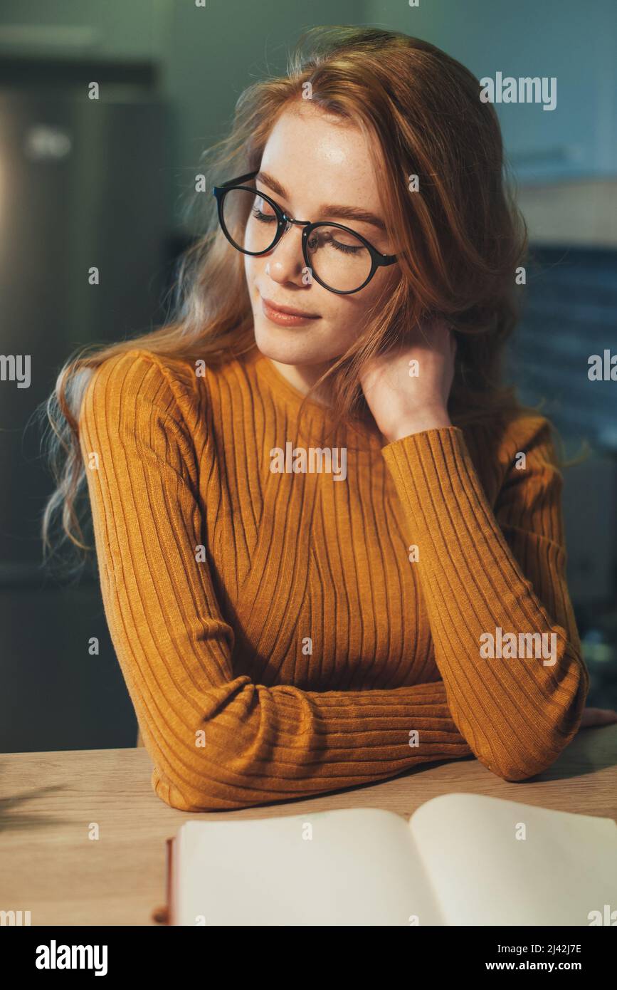 Scatto interno di una donna sognante zenzero che lavora sulla recensione del libro. Tempo libero con letteratura, concetto di hobby. Foto Stock