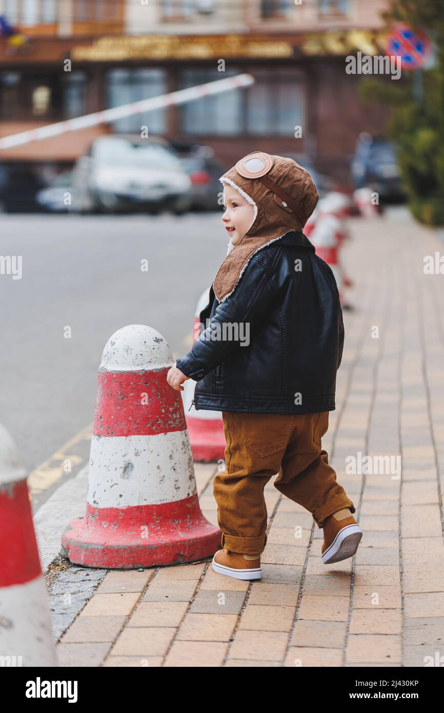 Ragazzo elegante 3 anni in una giacca di pelle e pantaloni marroni cammina per la strada. Bambino moderno. Moda per bambini. Buon bambino Foto Stock