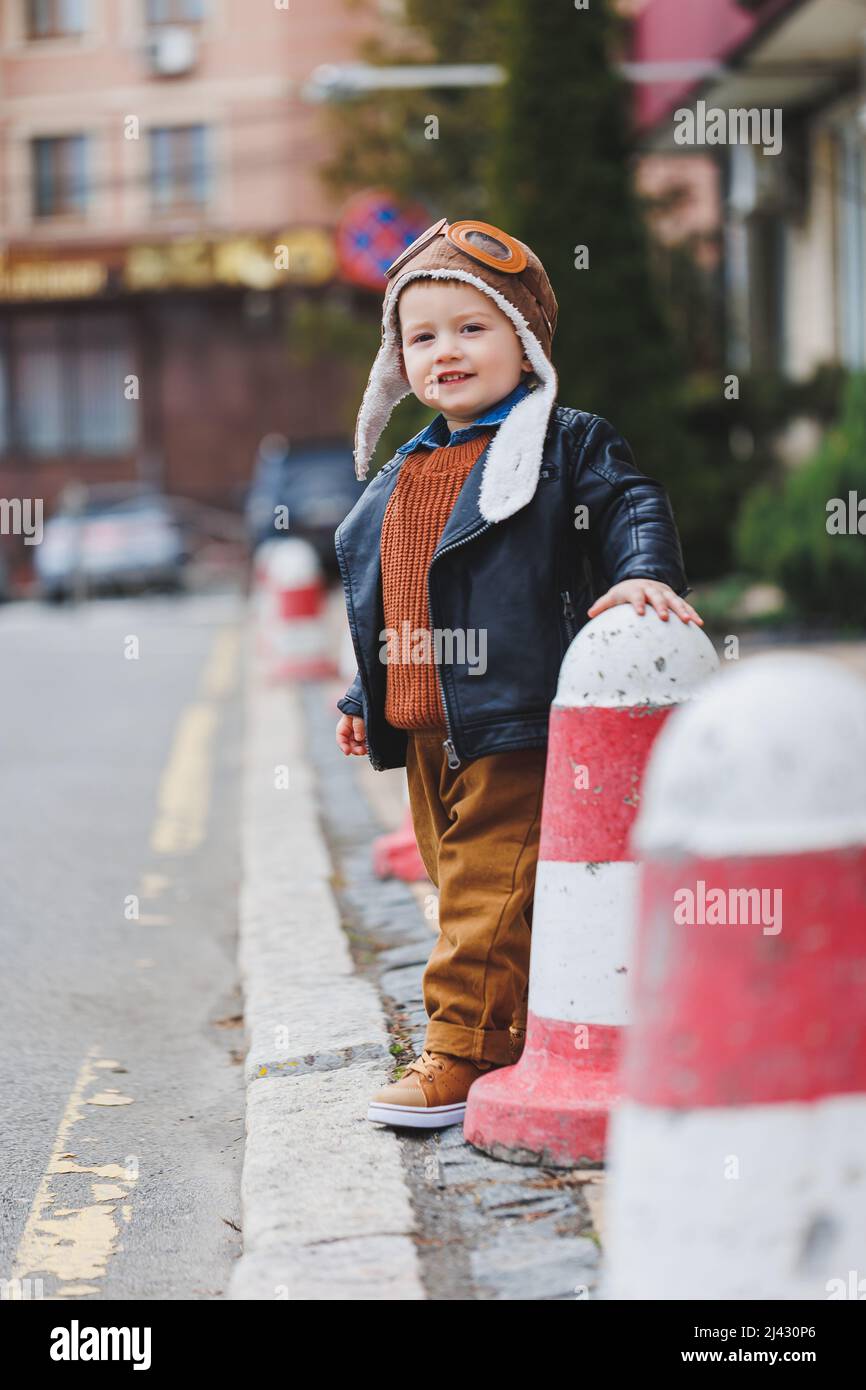 Ragazzo elegante 3 anni in una giacca di pelle e pantaloni marroni cammina per la strada. Bambino moderno. Moda per bambini. Buon bambino Foto Stock