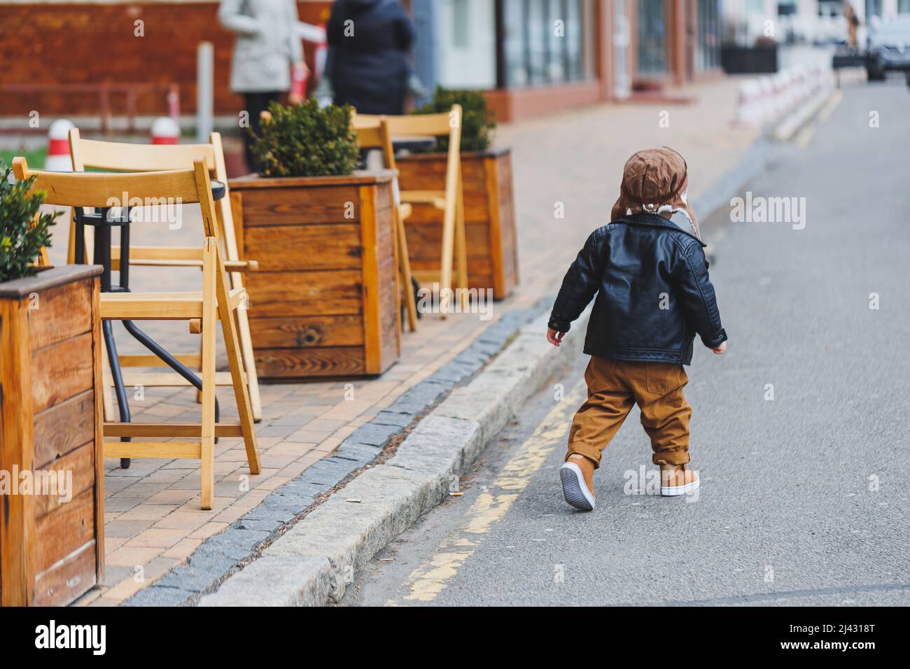 Ragazzo elegante 3 anni in una giacca di pelle e pantaloni marroni cammina per la strada. Bambino moderno. Moda per bambini. Buon bambino Foto Stock