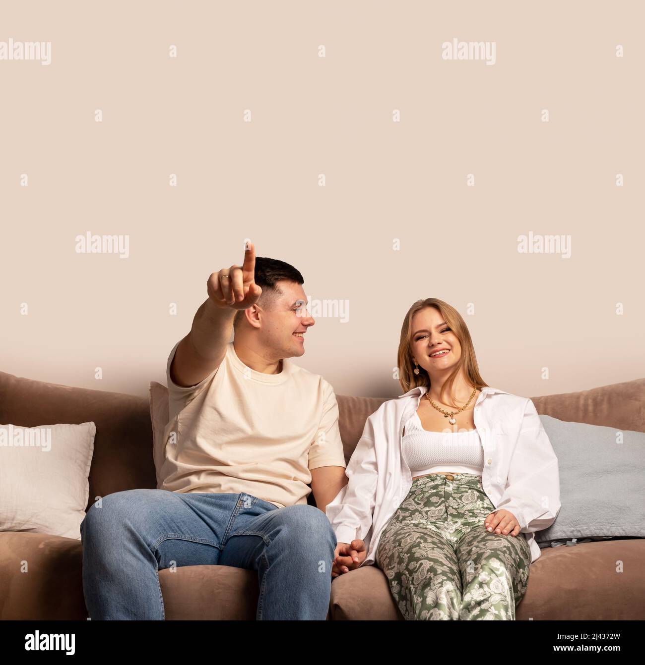 Coppia felice seduta sul divano, ridendo e guardando film commedia. Uomo che punta sullo schermo. Donna sorridente. Spazio di copia per il testo. Foto Stock