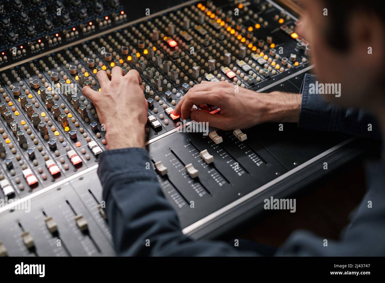 Primo piano dei pulsanti di comando e attivazione/attivazione delle mani maschili sulla workstation audio digitale in studio di registrazione, concetto di produzione musicale Foto Stock