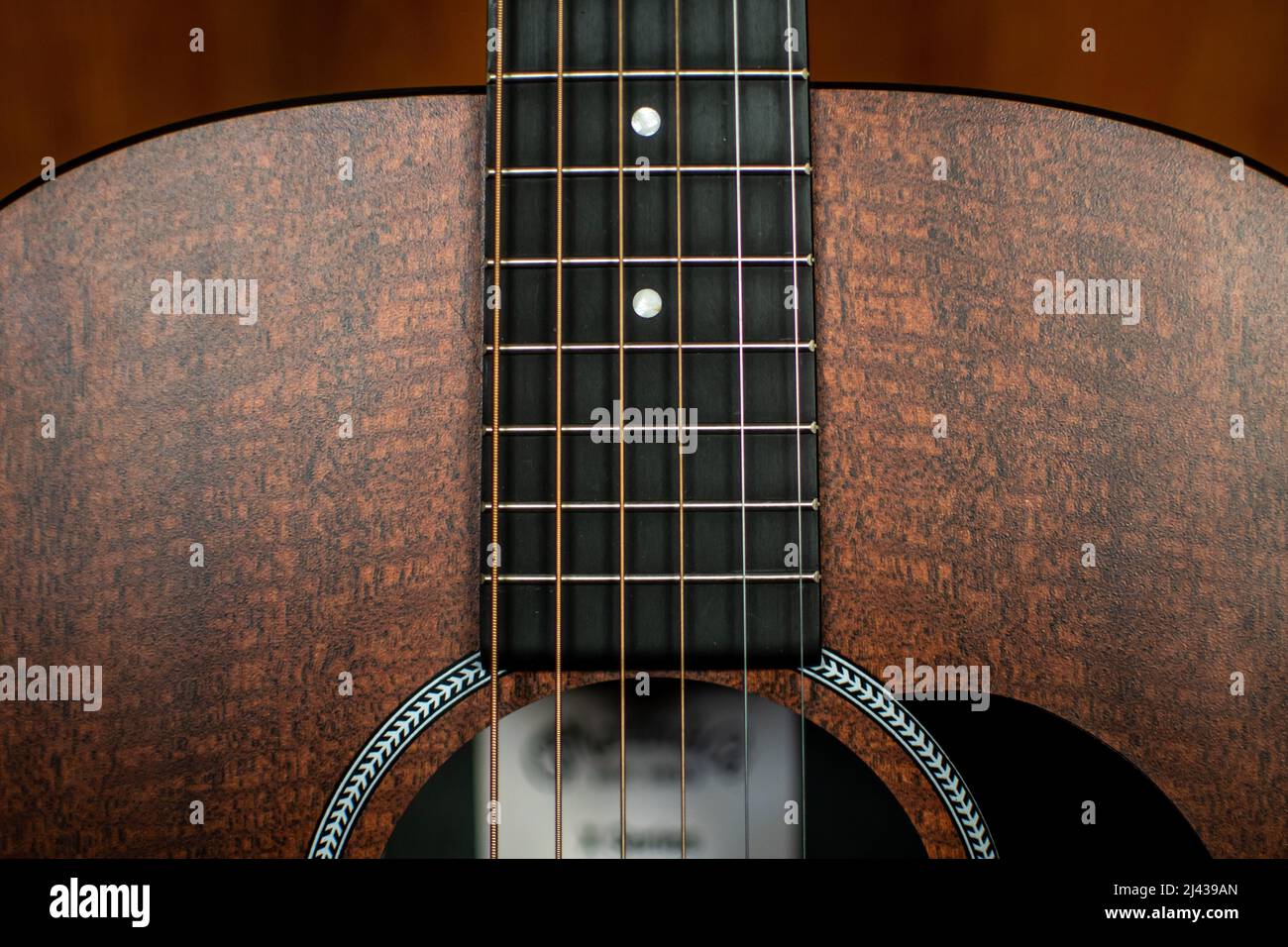 Un primo piano del corpo superiore di una chitarra acustica che mostra la tastiera, i tasti, i marcatori di posizione, le corde, la rosetta, pickguard e foro sonoro. Foto Stock