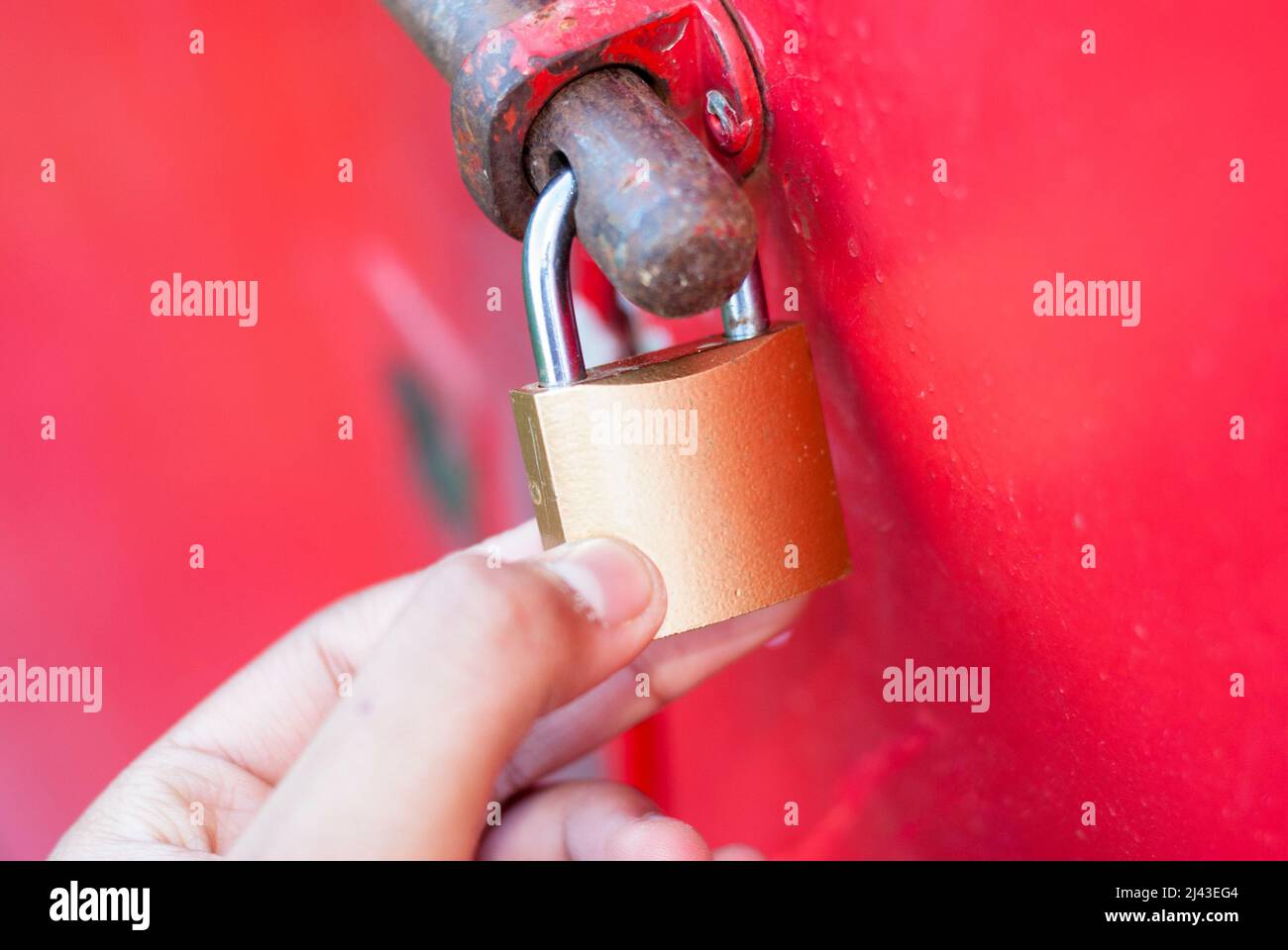 Mani che tengono chiuso lucchetto dorato sulla porta rossa orizzontale Foto Stock