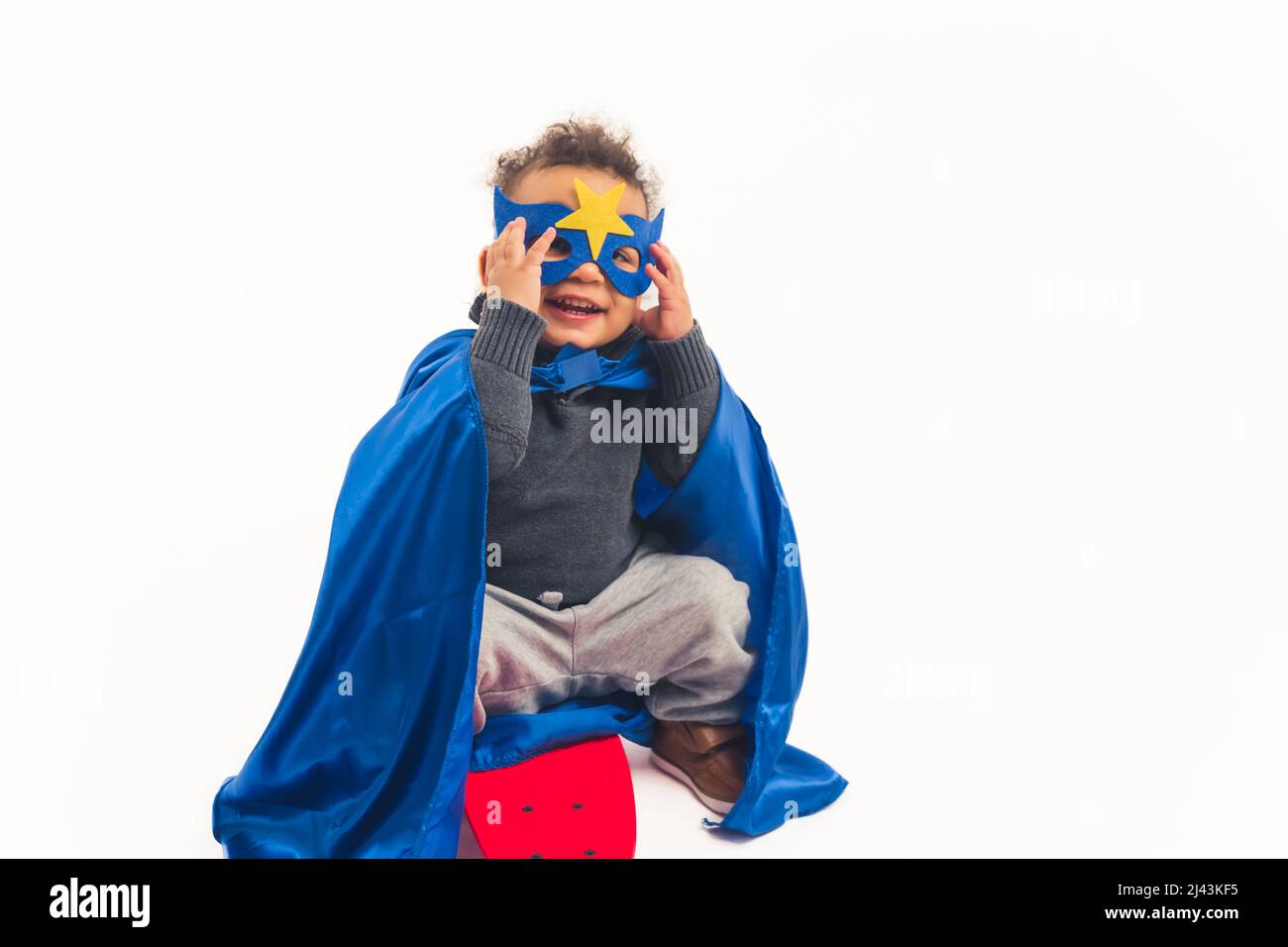 Carino afroamericano arricciato ragazzino con il costume di un supereroe sorridente e toccando il suo studio maschera girato full shot bianco sfondo copia spazio. Foto di alta qualità Foto Stock