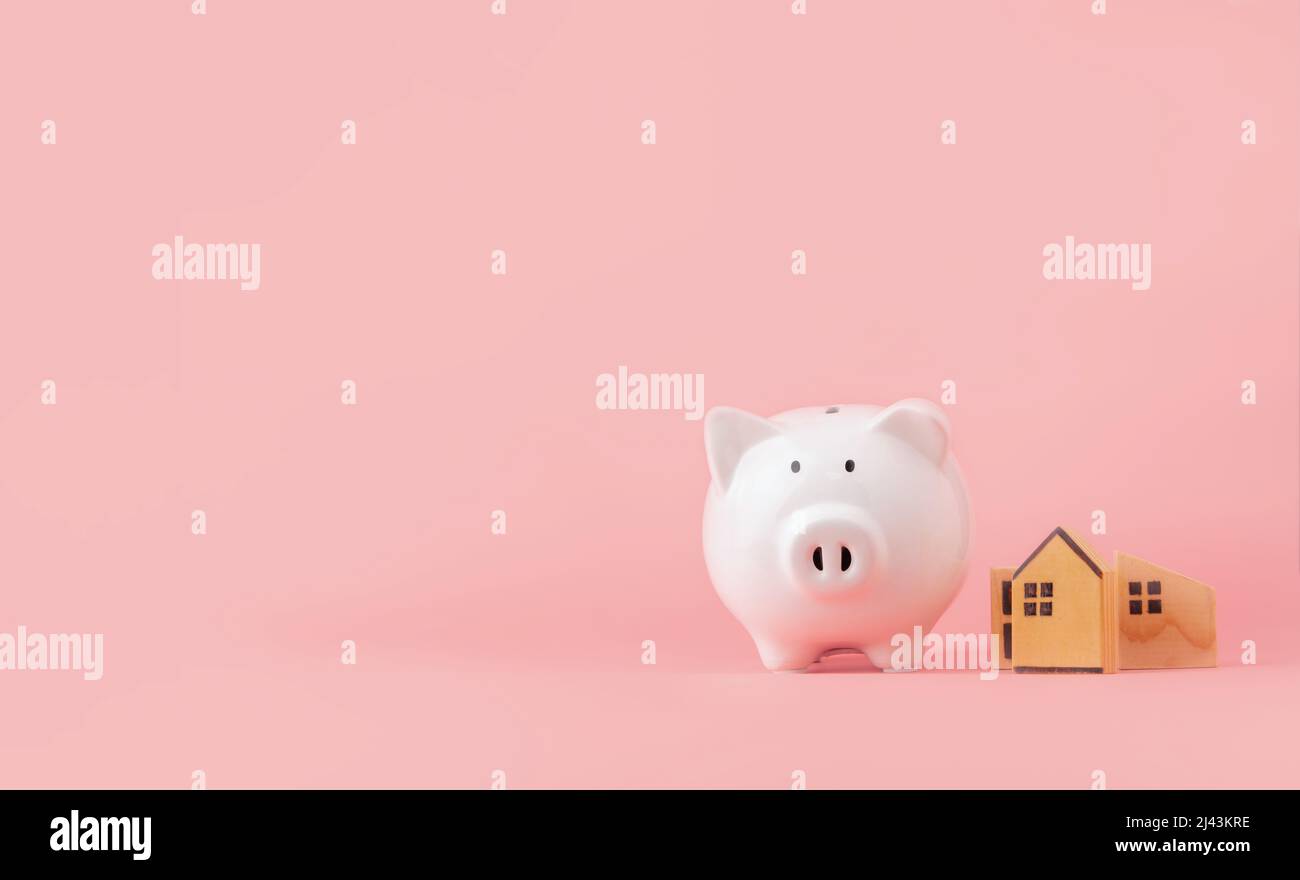 Risparmio di denaro e concetto di investimento. Piggy banca e casa in legno su sfondo rosa con spazio copia Foto Stock