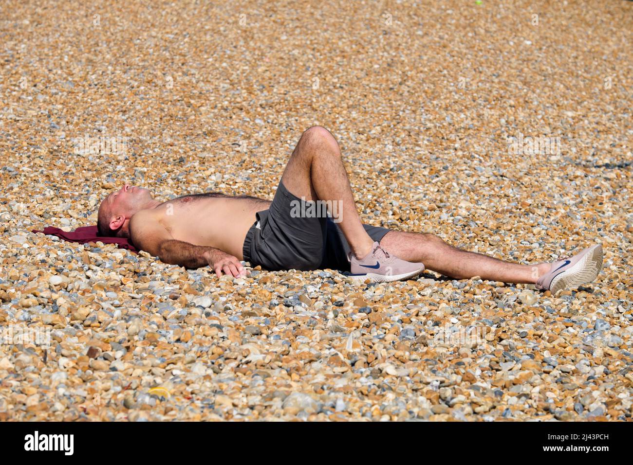 Un giovane uomo che ottiene un certo raggio come si sunbathes sulla spiaggia di ciottoli in Eastbourne East Sussex Inghilterra UK Foto Stock