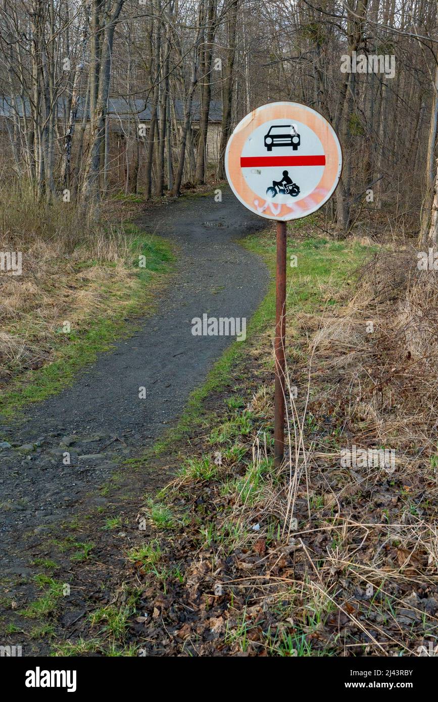 Non ci sono automobili e non ci sono motocicli accanto a un sentiero che conduce a una foresta in una giornata nuvolosa di primavera. Cartello stradale in zona rurale remota. Foto Stock