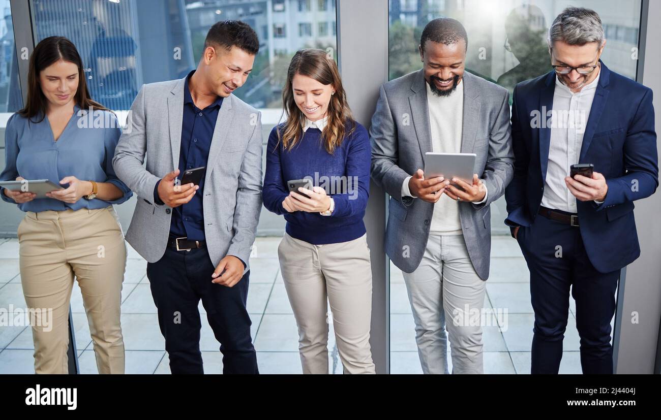 Theres sempre tempo per una risata rapida. Scatto di un gruppo di giovani imprenditori che utilizzano dispositivi digitali mentre attendono in linea. Foto Stock