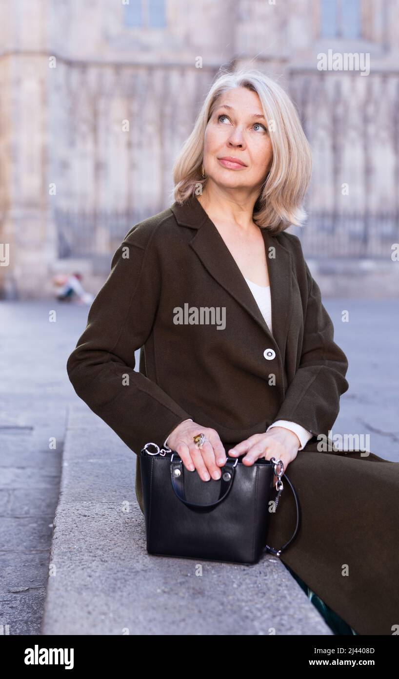 Positivo donna matura si siede sulla scalinata di pietra nella città vecchia Foto Stock