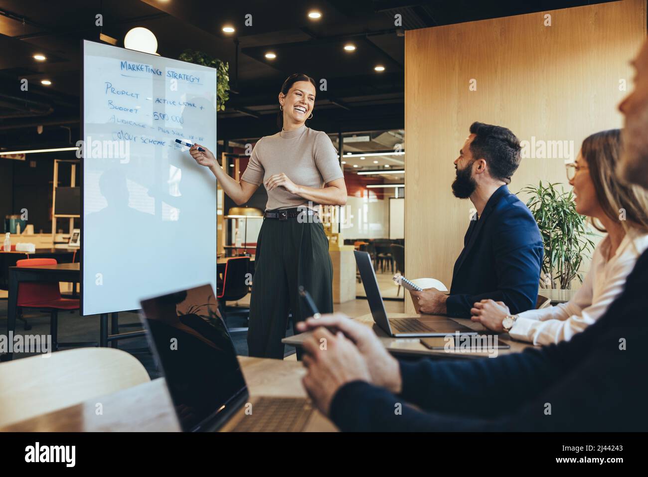 Un manager aziendale allegro che offre una presentazione in un ambiente di lavoro moderno. Felice giovane donna d'affari sorridente mentre presenta la sua strategia di vendita Foto Stock