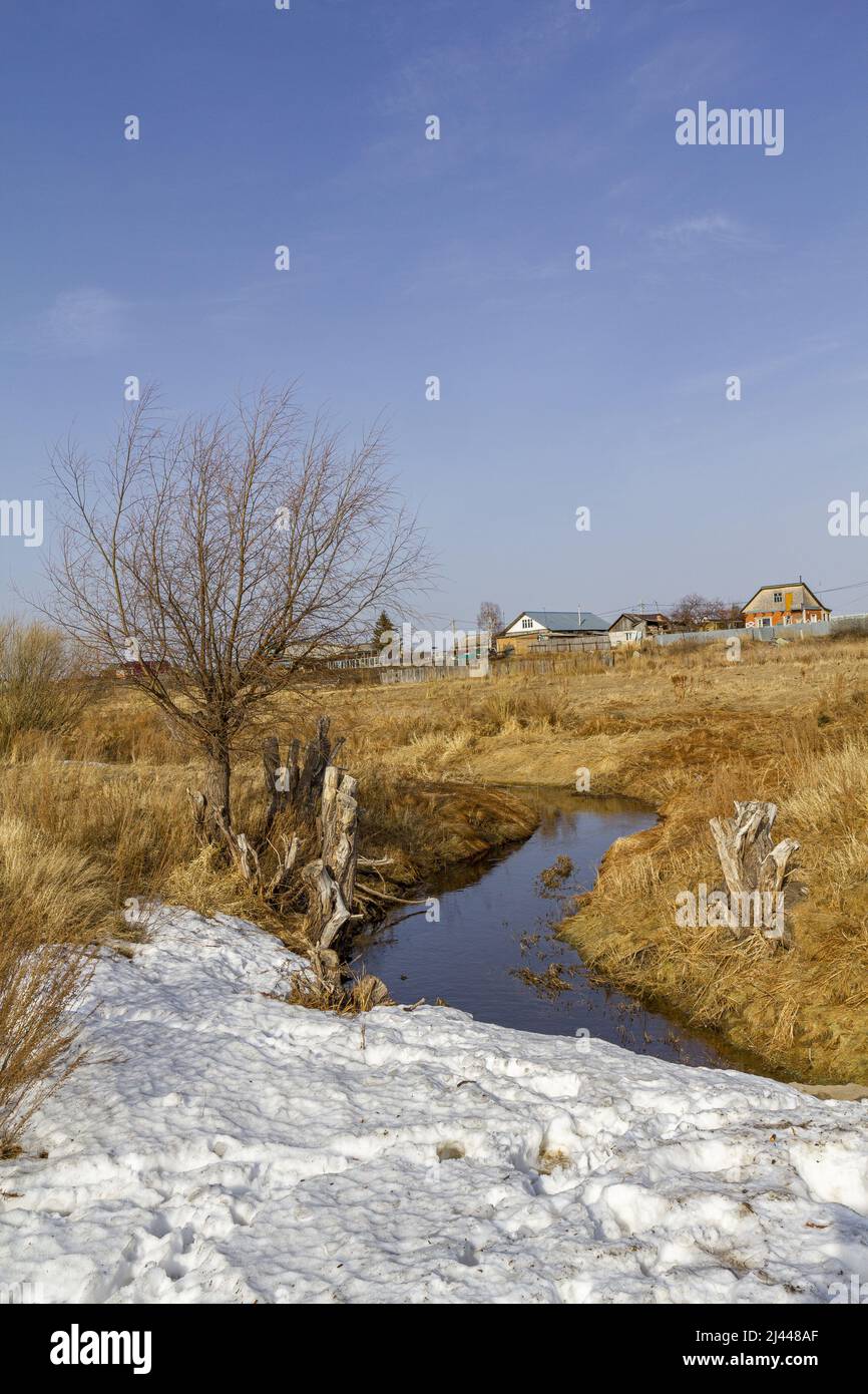 Paesaggio con vista su un fiume tortuoso con coste, erba giurata sullo sfondo del villaggio. Foto Stock