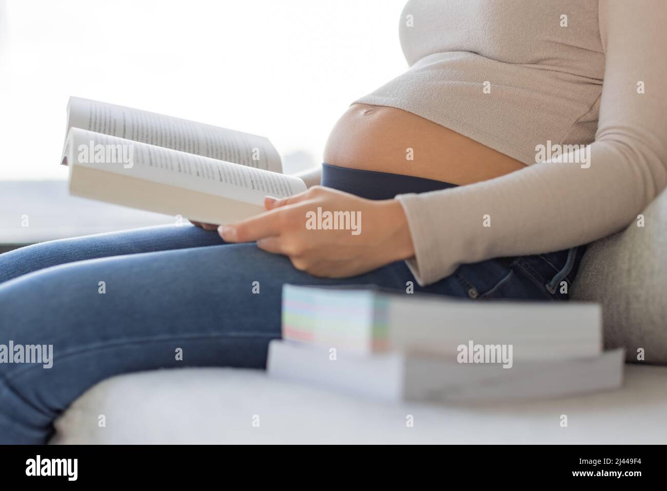 Libro prenatale che legge la donna incinta che tiene i libri seduti sul divano a casa. Gravidanza stile di vita preparazione per la nascita e l'innalzamento di un bambino Foto Stock