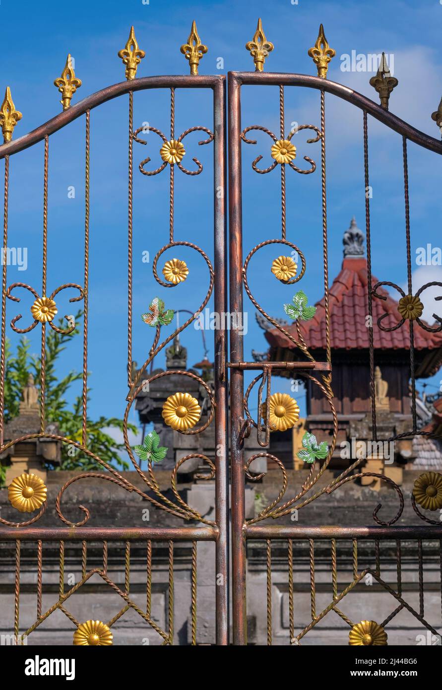 Vista attraverso il cancello di ottone con emblemi floreali al tempio balinese con sfondo cielo blu Foto Stock