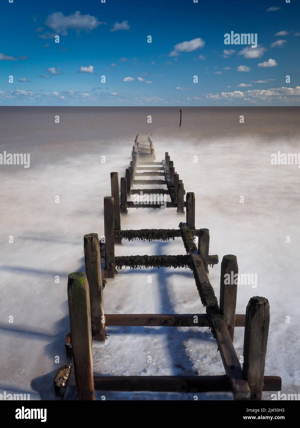 Lunga esposizione di onde che rotolano su legno groyne, Overstrand Beach, Norfolk, UK Foto Stock