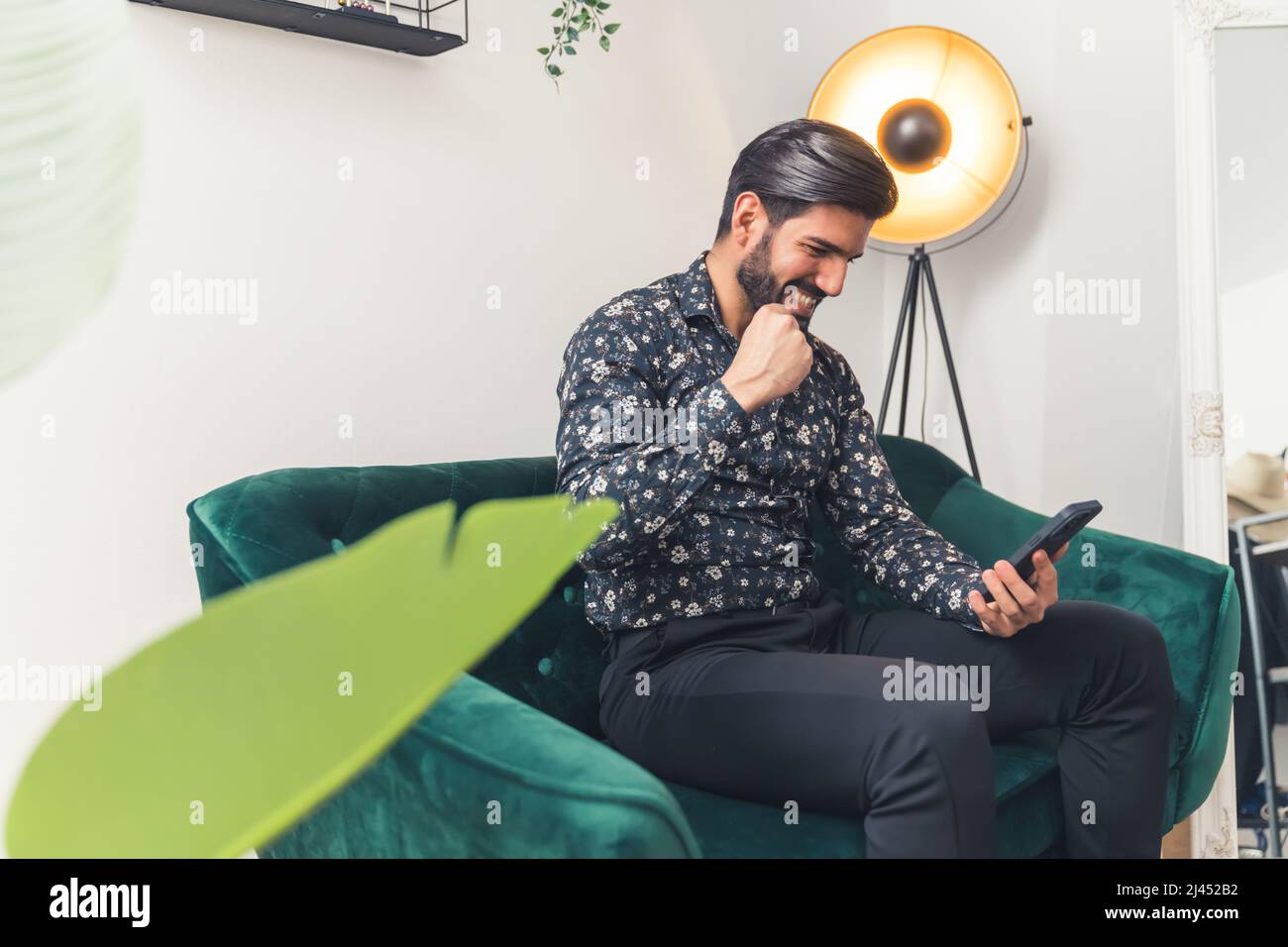 l'uomo felice leggendo le buone notizie nel suo telefono mobile e celebrando il concetto di successo medio full shot indoor. Foto di alta qualità Foto Stock